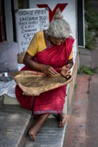 Woman in red sari sorting pepper corns in a whicker tray outside her shop